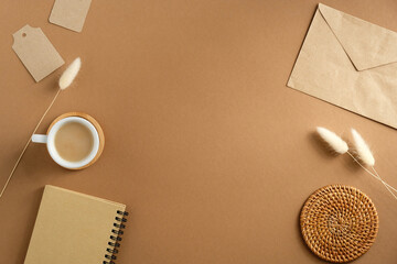 Wall Mural - Elegant feminine workspace with cup of coffee, paper envelope, notebook, dry flowers on brown background. Vintage home office desk table, top view.