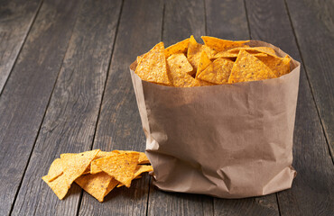 Corn tortilla chips or nachos spilling out of the large package on a wooden table.