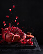 Freeze motion of sliced pomegranate red fruit with splashing juice, drops and seeds on black background. Copy space.