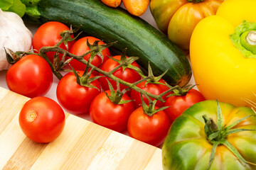 Wall Mural - Red cherry tomatoes with cucumbers, peppers and garlic on a wooden kitchen cutting board