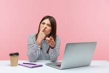 You Are Liar! Bossy Woman Office Worker Sitting At Workplace, Touching Nose And Pointing To Camera, Blaming Liar In Deception, Suspecting Falsehood. Indoor Studio Shot Isolated On Pink Background