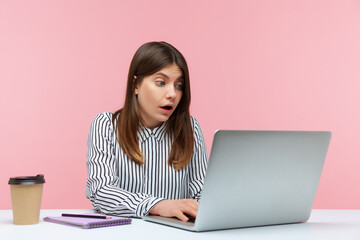 Wall Mural - Surprised excited woman office worker in striped shirt looking at laptop with big eyes and open mouth, reading shocking news or talking on video call. Indoor studio shot isolated on pink background