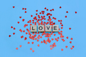 Poster - Word Love decorated with red confetti hearts on blue background. Valentine's day postcard. Selective focus