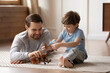 Smiling young Caucasian dad and little preschooler son sit on floor at home play together with toys. Happy caring father have fun feel playful engaged in game activity with small boy child on weekend.