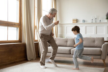 Excited Elderly Grandfather Have Fun Dance With Little Preschooler Grandson In Living Room At Home. Overjoyed Mature Granddad Enjoy Family Weekend Listen To Music With Small 6s Boy Child.
