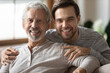 © fizkes - Close up portrait of smiling millennial man with mature father hug and cuddle enjoy family weekend at home. Happy young Caucasian adult son show love and care feel grateful to elderly 70s dad.