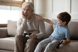 © fizkes - Mature Caucasian grandfather and little preschooler grandson play computer video games together. Happy small boy child make fun laugh at sad grandparent losing in funny childish activity.