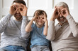 © fizkes - Portrait of overjoyed three generations of men make funny facial expressions gestures relaxing at home together. Happy boy with young father and elderly grandfather have fun rest enjoy family weekend.