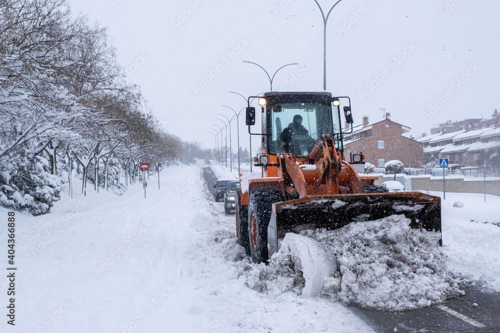 A snowplow removes the snow from a street in a residential area, two cars drive behind it. Effects of the Filomena snowstorm - obrazy, fototapety, plakaty 