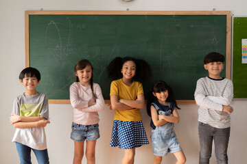 happy multiethnic children in casual clothes crossing arms and smiling while standing near chalkboar