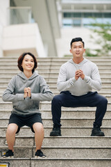 Poster - Cheerful young Vietnamese couple doing squats together after running on city streets in the morning