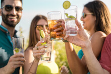 Group Of Young People Clinking Cocktail Glasses Outdoors In The Summer. Gathering Of Friends Enjoying Time Together At Outdoors Cafe Drinking Alcoholic Drinks