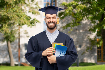 Poster - education, graduation and people concept - happy smiling male graduate student in mortar board and bachelor gown with books over university campus background