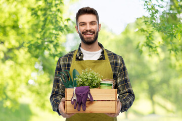 Sticker - gardening, farming and people concept - happy smiling male gardener or farmer in apron with box of garden tools over green natural background