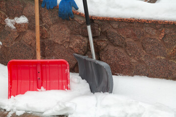 Two plastic snow shovels stand in front of  fence