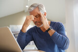 Fototapeta  - Senior man having a headache while working on laptop computer