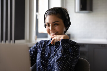 Poster - Close up of smiling millennial Indian woman in earphones look at laptop screen talk on webcam call. Happy young ethnic female in headphones have video digital virtual conversation on computer online.