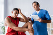 © LIGHTFIELD STUDIOS - chiropractor holding digital tablet near upset african american man in sportswear in clinic