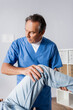 © LIGHTFIELD STUDIOS - mature masseur working with injured knee of patient in clinic