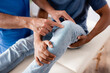 partial view of mature chiropractor pointing with finger at knee of african american patient on massage table