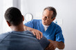 © LIGHTFIELD STUDIOS - chiropractor working with injured arm of african american man on blurred foreground