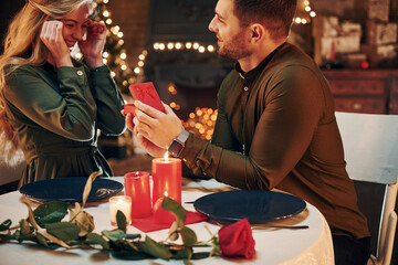 Man proposing a beautiful woman to marry him in an elegant restaurant. Young lovely couple have romantic dinner indoors together