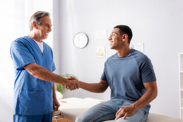happy chiropractor shaking hands with african american patient