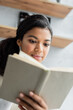 © LIGHTFIELD STUDIOS - young african american woman reading book at home on blurred foreground