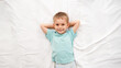 © Кирилл Рыжов - Top view portrait of smiling little boy lying on white sheets on the bed and looking in the camera. Concept of happy children having good time at home