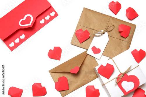 Envelope from red paper with hearts, white gift box with red label in a heart form, gift wrapped in brown craft paper, tied with twine with a bow, envelope from craft paper with red heart on white 