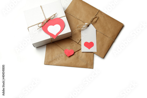 White gift box with red label in a heart form, gift wrapped in brown craft paper, tied with twine with a bow, envelope from craft paper with red heart on white background isolated 