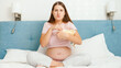 Concentrated pregnant woman watching movie on TV and eating popcorn from big bowl