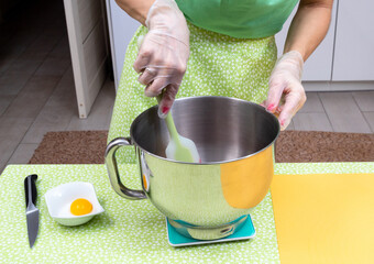 Wall Mural - Women's hands holding a silicone spatula mix ingredients for dessert in a metal bowl. Next to it is a knife and an egg yolk.