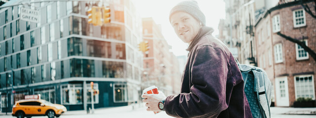 Wall Mural - Smiling man with coffee cup on the crossroad walking in the city. Wide screen, panoramic