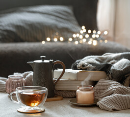 Wall Mural - Cozy home composition with cup of tea, teapot, candlestick and books on blurred background.