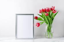 Bouquet Blooming Pink White Tulip Flowers In Glass Vase And Empty Poster Or Photo Frame Mockup On White Marble Table In Interior.