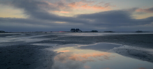 Landscape view of a beach and stilt houses with cloud reflexion in mud flat, St Peter-Ording, North Friesland, Germany, Europe.