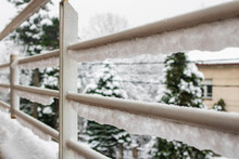 View Through White Balcony Fence Under The Snow With Pine Trees In The Background, Winter In A City