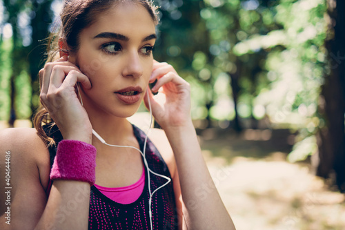 Portrait of female runner standing in nature and putting earphones in ears.