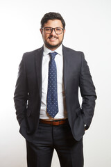 A young Latino businessman wearing glasses and standing in a dark suit and tie on a white background