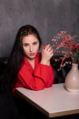 sexy attractive brunette woman in red blouse and black skirt in a loft vintage cafe near a vase with decorative sparkling red branches. st valentines .