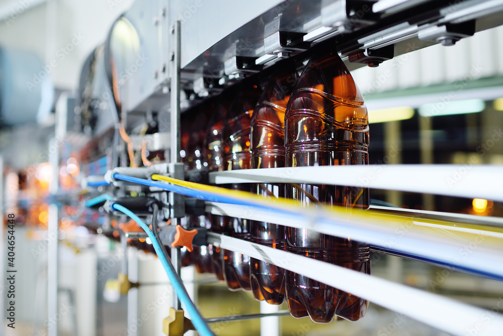 Industrial production of plastic bottles for low-alcohol beverages, soda and sunflower oil. Empty PET bottles of brown color on the background of modern equipment. - obrazy, fototapety, plakaty 