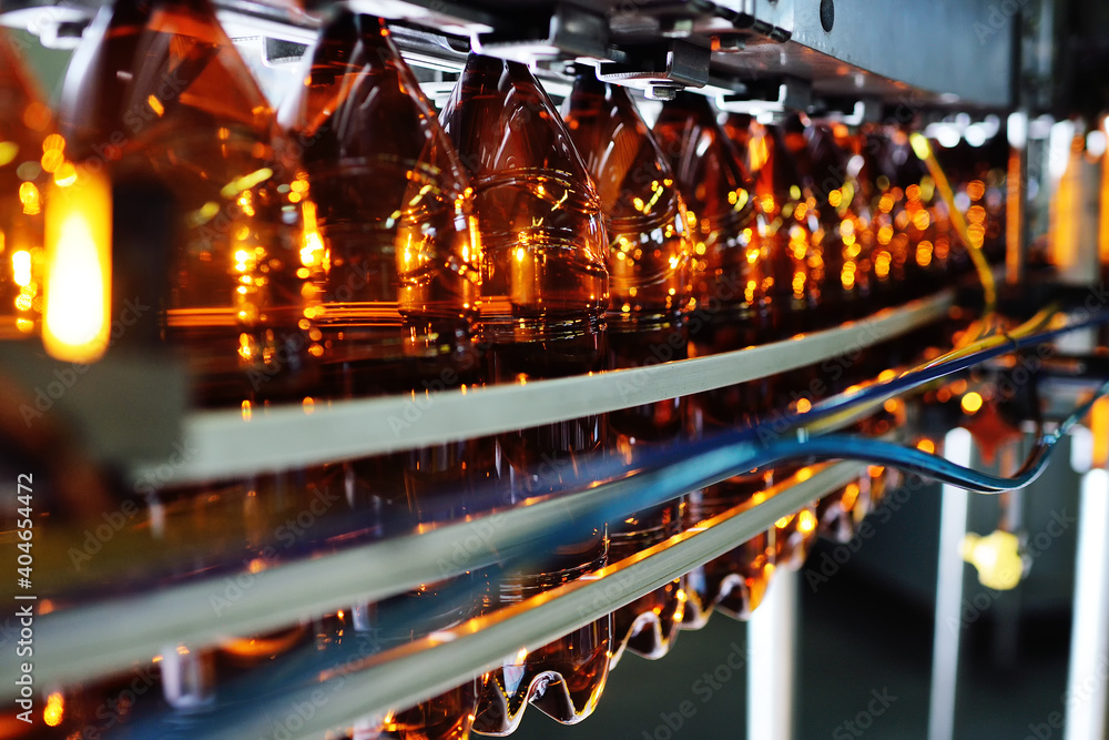 Industrial production of plastic bottles for low-alcohol beverages, soda and sunflower oil. Empty PET bottles of brown color on the background of modern equipment. - obrazy, fototapety, plakaty 