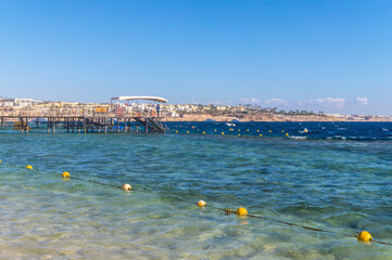 Wall Mural - Sharm el sheikh / Egypt - December 03 2019: Wooden pier on the tourist coast of the Red Sea in the city of Sharm El Sheikh on the Sinai Peninsula in Egypt. Sea bay and Tiran island on the horizon