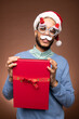 © pressmaster - Happy young mixed-race man in xmas eyewear and Santa cap holding red giftbox
