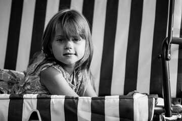 Wall Mural - Portrait of little girl lying on a swing in the yard of a country house. Black and white photo.