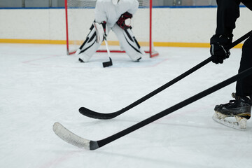 Hockey sticks held by two players in sports uniform on background of goal keeper