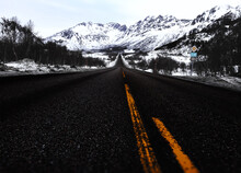 Empty Road Leading Towards Snow Covered Mountains
