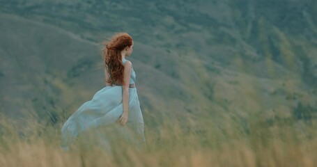 Wall Mural - Beautiful girl with red hair in white dress looking at landscape in mountains while wind blows her hair - freedom, inspiration cinematic 4k footage