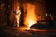 Foundry worker in aluminized protective fire suit checking temperature of molten iron in furnace. Industrial steel production and metallurgy.